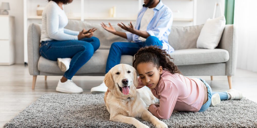 Sad girl embracing dog, parents fighting in the background