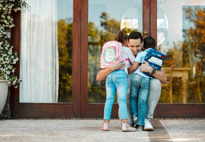 Children returning from school and hugging father on their return. Daddy missed little daughter and son holding children in arms hugging girl and boy while standing by the door