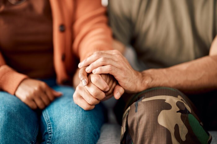 Marriage, holding hands and couple on sofa in therapy for argument, problem advice and divorce counseling. Psychology, mental health and woman with military man on couch for ptsd, help and support