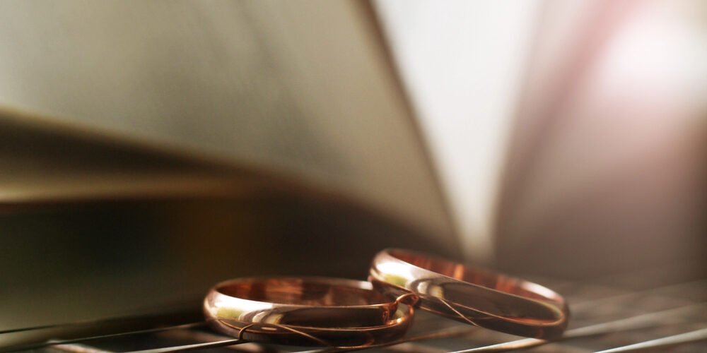 Protecting Wealth- Key Strategies for High-Asset Divorces in New Jersey Two gold wedding rings placed on a reflective surface with a blurred open book in the background, symbolizing divorce and legal strategies.
