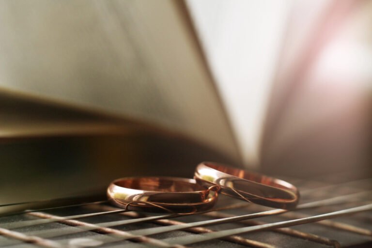 Protecting Wealth- Key Strategies for High-Asset Divorces in New Jersey Two gold wedding rings placed on a reflective surface with a blurred open book in the background, symbolizing divorce and legal strategies.