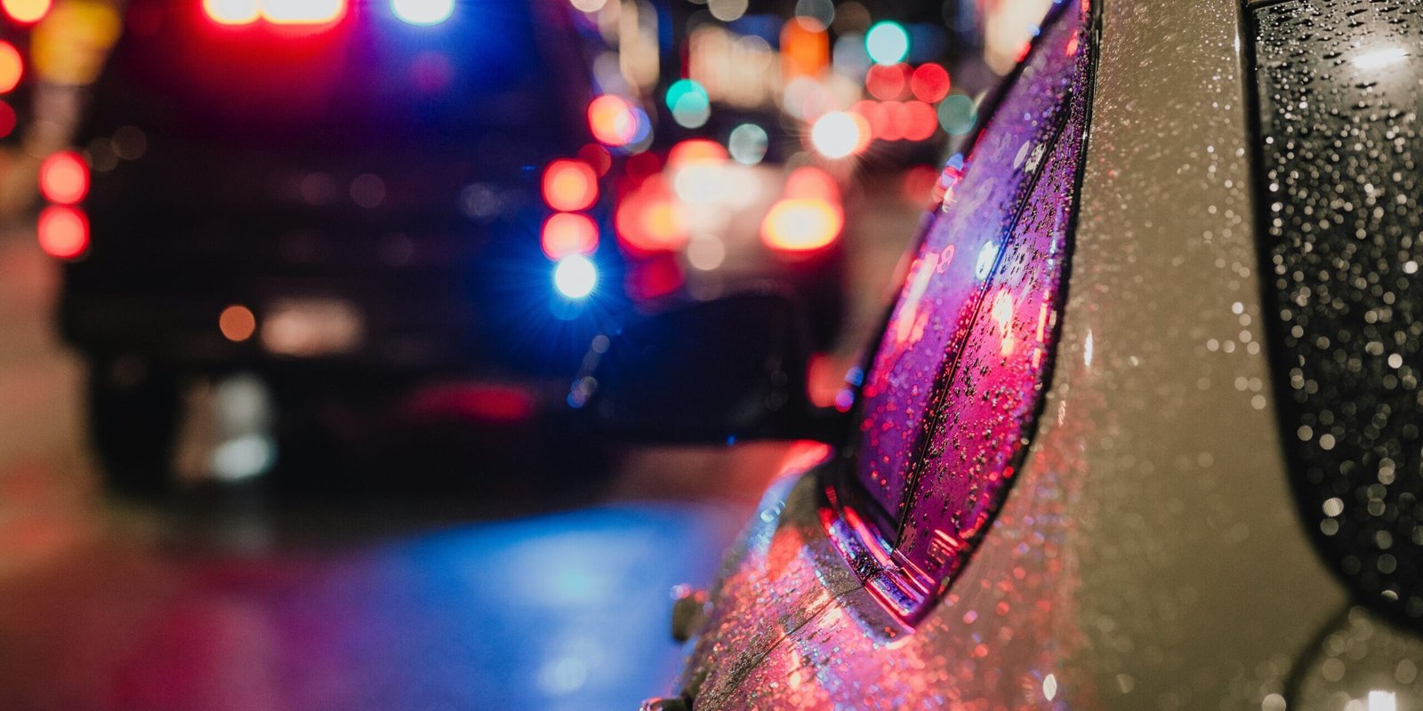 albert-stoynov-PiEBY75vv5Q-unsplash Police car in rain at night with lights on.