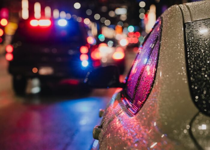 albert-stoynov-PiEBY75vv5Q-unsplash Police car in rain at night with lights on.