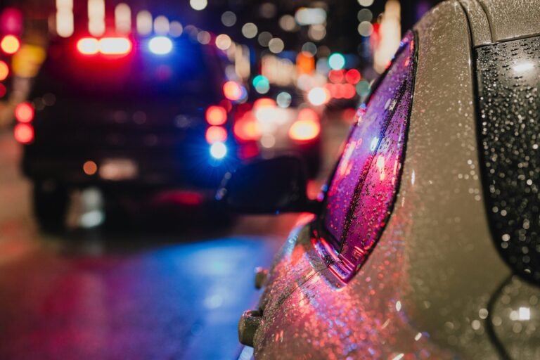Police car in rain at night with lights on.